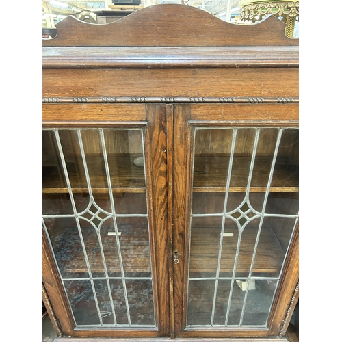 172 - An early 20th century oak display cabinet with two lead and stained glass doors on barley twist supp... 