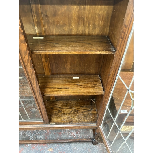 172 - An early 20th century oak display cabinet with two lead and stained glass doors on barley twist supp... 