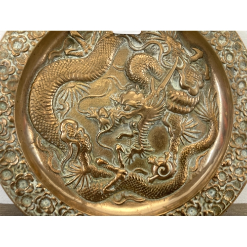 427B - An antique Oriental cast brass shallow bowl with dragon design and floral border - approx. 23.5cm di... 