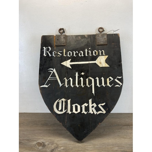 550 - A wooden shield shaped hand painted restoration, antiques and clocks double sided advertising sign -... 