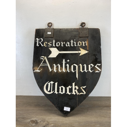 550 - A wooden shield shaped hand painted restoration, antiques and clocks double sided advertising sign -... 