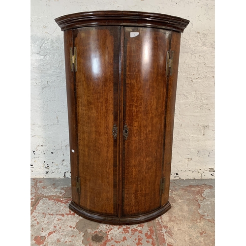 86 - A George III oak and mahogany crossbanded bow fronted wall hanging corner cabinet with brass H hinge... 