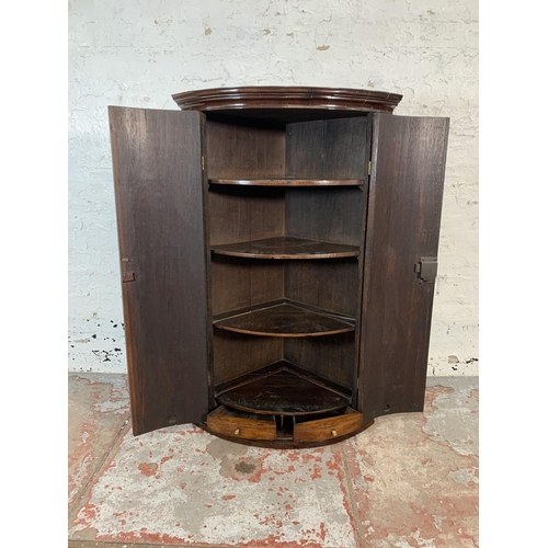 86 - A George III oak and mahogany crossbanded bow fronted wall hanging corner cabinet with brass H hinge... 