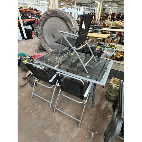 959 - A grey metal and smoked glass six piece patio set comprising table and five folding chairs - table a... 