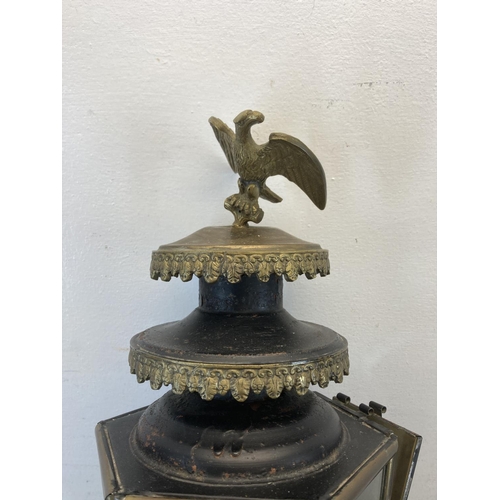 463 - A late 19th/early 20th century brass and black metal carriage lamp with eagle design top and later a... 