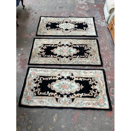 93 - Three black and cream floral pattern rugs - approx. 150cm x 72cm