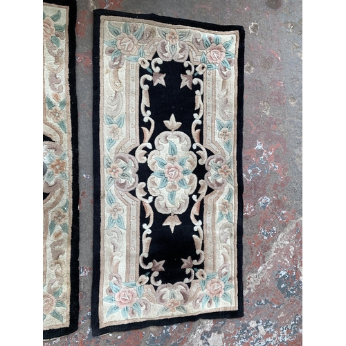 93 - Three black and cream floral pattern rugs - approx. 150cm x 72cm