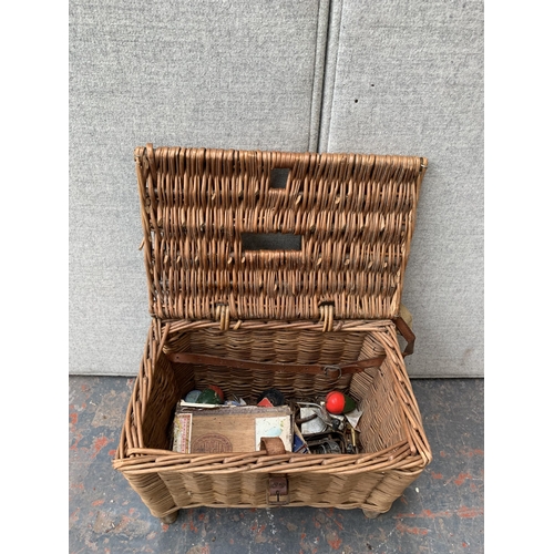 864 - A wicker fishing basket containing fishing tackle to include landing net, reels, floats etc.