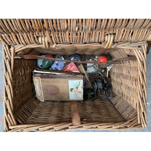 864 - A wicker fishing basket containing fishing tackle to include landing net, reels, floats etc.