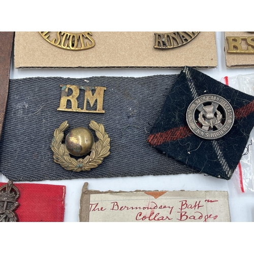 2162 - A collection of military badges and shoulder titles to include Royal Scots, Royal Marines etc.