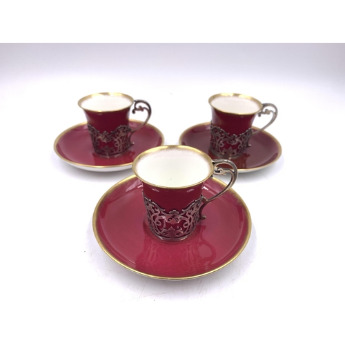 344 - Three Aynsley red and gold glazed cups and saucers with hallmarked London silver holders - approx. g... 