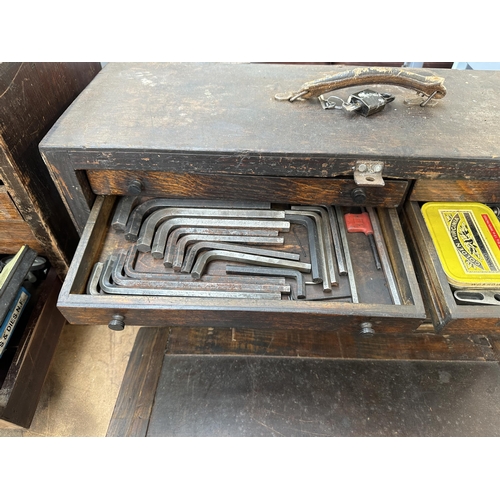 1052 - An early 20th century oak engineer's tool cabinet containing various tap and die sets, spanners etc.