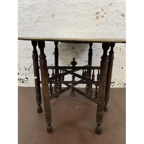 130 - A Middle Eastern carved hardwood and embossed brass travel table - approx. 55cm high x 78cm diameter