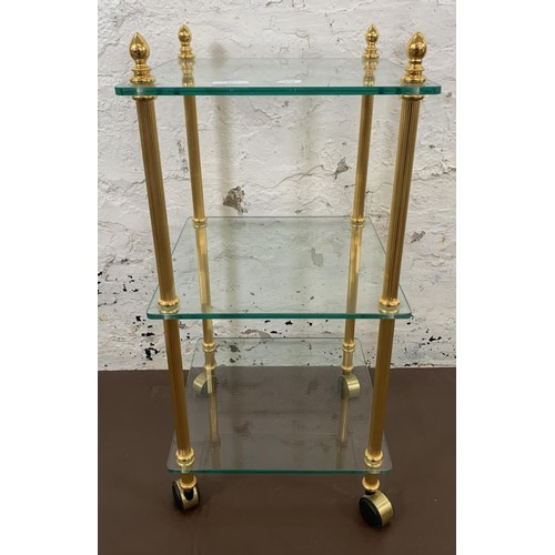 55 - A vintage brass effect and glass three tier side table - approx. 70cm high x 33cm wide