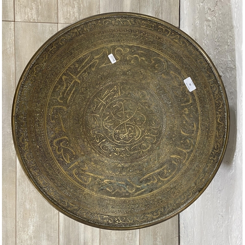 26 - An Indian Benares brass circular topped occasional table on wooden folding stand, registered design ... 