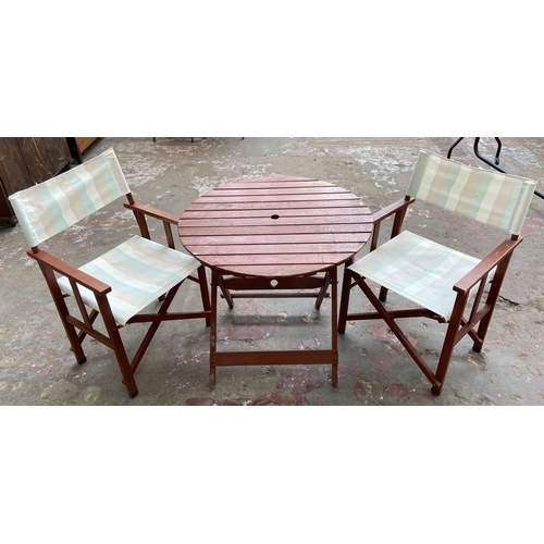 100 - A stained teak three piece patio set comprising circular folding table and two chairs - table approx... 