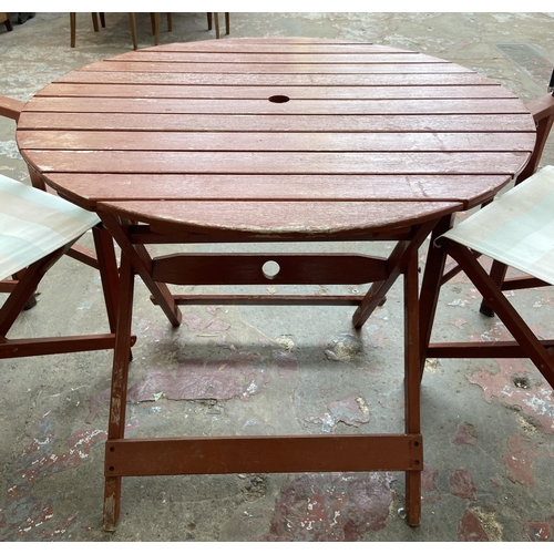 100 - A stained teak three piece patio set comprising circular folding table and two chairs - table approx... 