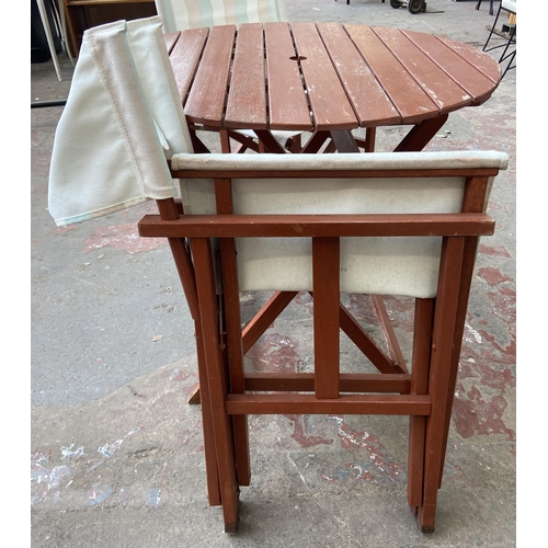 100 - A stained teak three piece patio set comprising circular folding table and two chairs - table approx... 