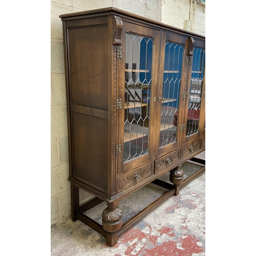 32 - A 17th century style carved oak four door display cabinet on baluster supports - approx. 155cm high ... 