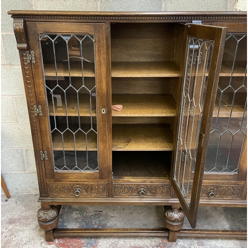 32 - A 17th century style carved oak four door display cabinet on baluster supports - approx. 155cm high ... 