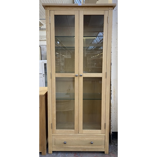 141 - A light oak display cabinet with one lower drawer, two glazed doors and four internal shelves - appr... 