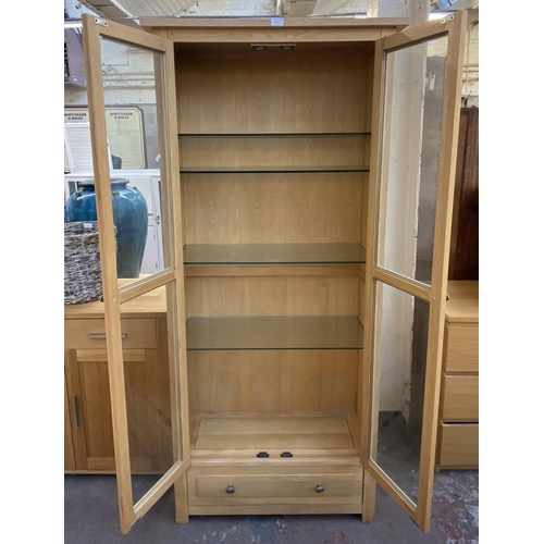 141 - A light oak display cabinet with one lower drawer, two glazed doors and four internal shelves - appr... 