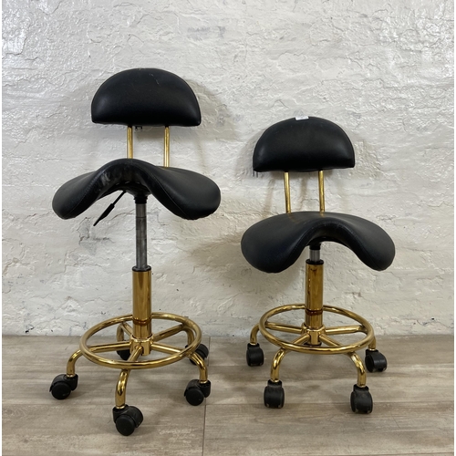 78 - A pair of black faux leather and gilt metal swivel saddle chairs