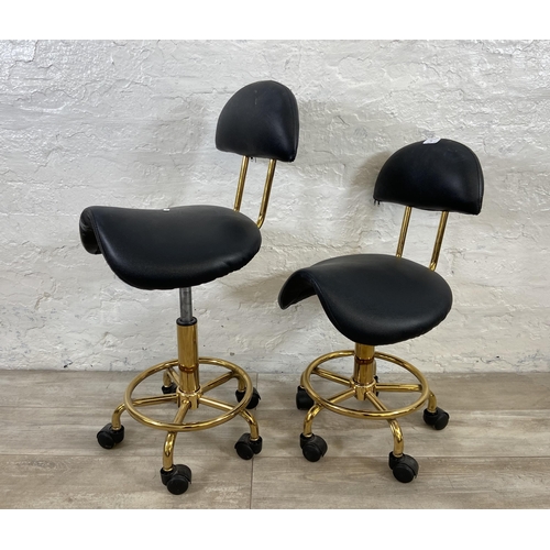 78 - A pair of black faux leather and gilt metal swivel saddle chairs