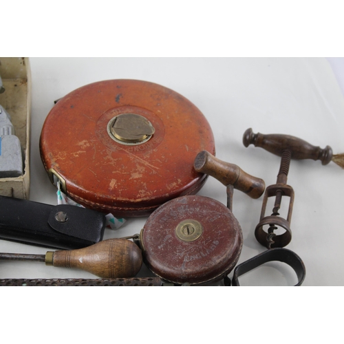 562 - A collection of vintage tools to include leather tape measures, corkscrew, spirit level etc.