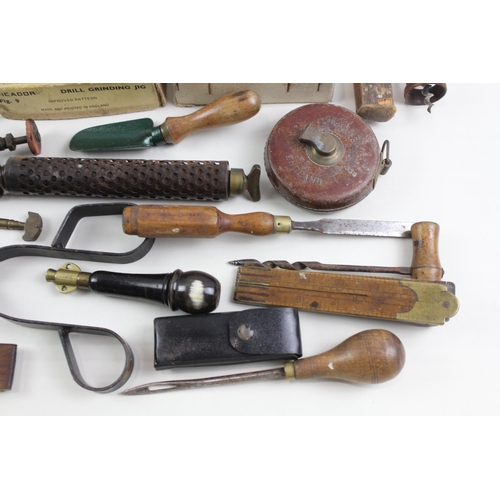 562 - A collection of vintage tools to include leather tape measures, corkscrew, spirit level etc.