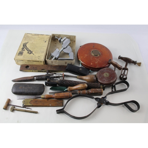 562 - A collection of vintage tools to include leather tape measures, corkscrew, spirit level etc.