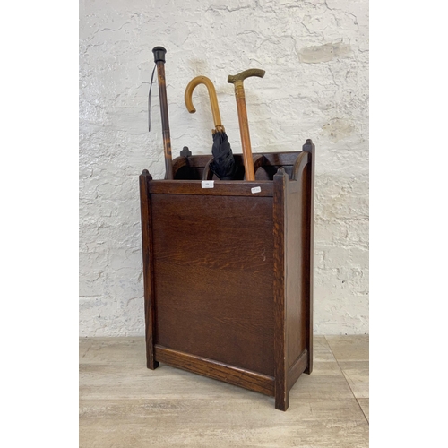 173 - An early 20th century oak six section stick stand containing two walking canes and one umbrella - ap... 