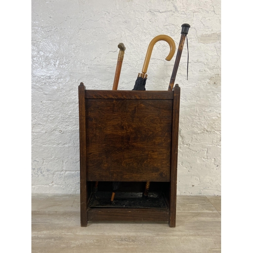 173 - An early 20th century oak six section stick stand containing two walking canes and one umbrella - ap... 