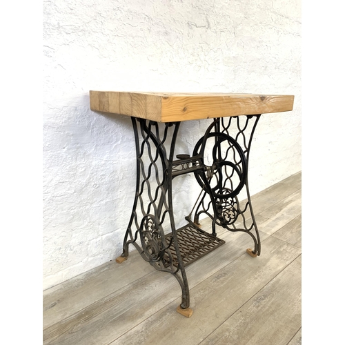 36 - An early 20th century black painted wrought iron treadle sewing machine base with later added pine r... 