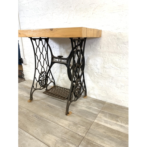 36 - An early 20th century black painted wrought iron treadle sewing machine base with later added pine r... 