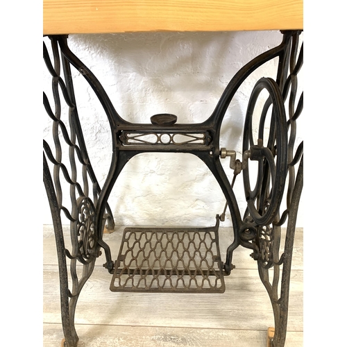 36 - An early 20th century black painted wrought iron treadle sewing machine base with later added pine r... 