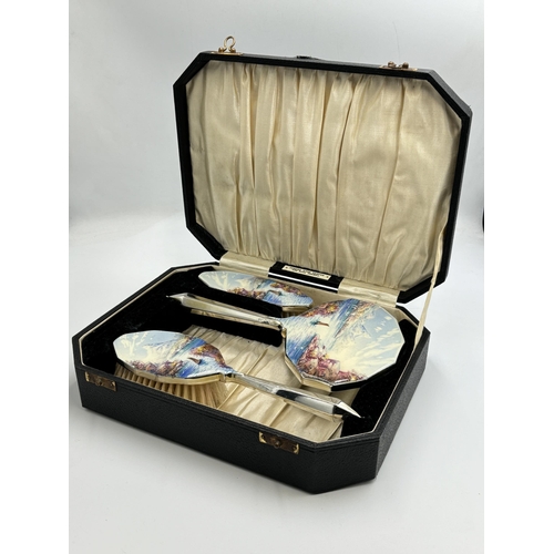 2165 - A cased Art Deco hand painted enamel and white metal three piece dressing table set