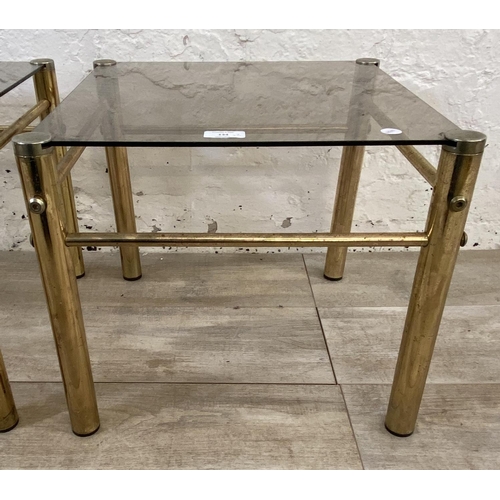 134 - A pair of Hollywood Regency style brass and smoked glass side tables - approx. 37cm high x 42cm wide... 