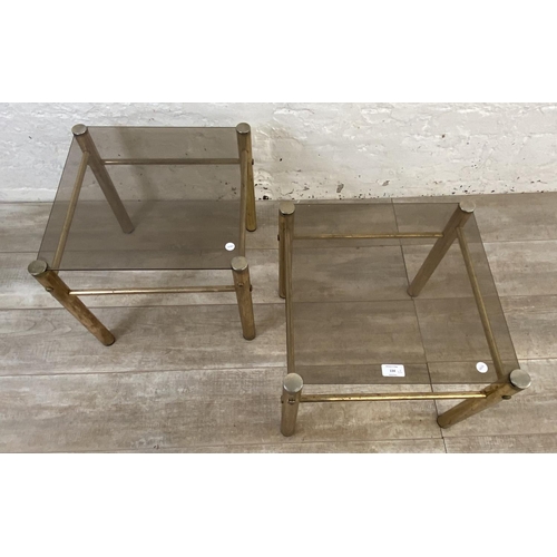 134 - A pair of Hollywood Regency style brass and smoked glass side tables - approx. 37cm high x 42cm wide... 