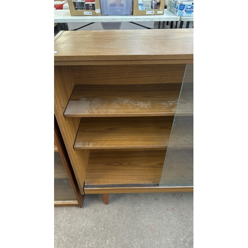 13D - A mid 20th century teak effect bookcase with two glass sliding doors - approx. 100cm high x 130cm wi... 