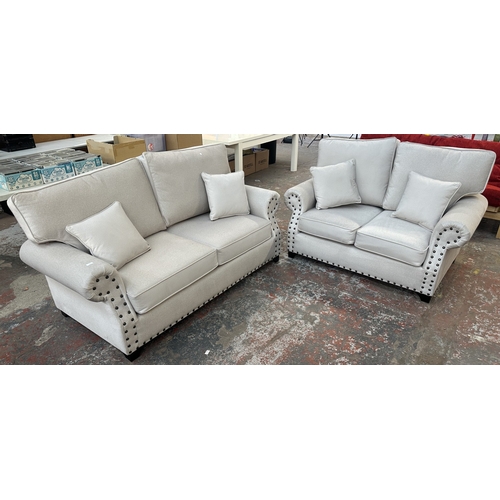 16 - A modern grey fabric upholstered and metal studded two piece lounge suite comprising two seater sofa... 