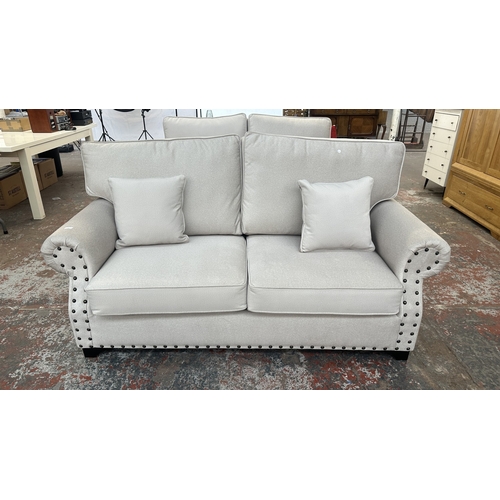 16 - A modern grey fabric upholstered and metal studded two piece lounge suite comprising two seater sofa... 