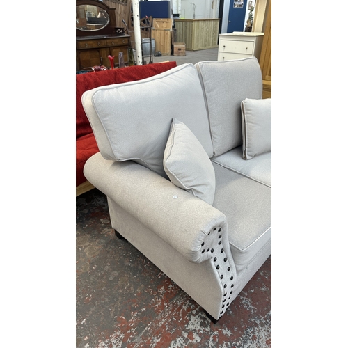 16 - A modern grey fabric upholstered and metal studded two piece lounge suite comprising two seater sofa... 