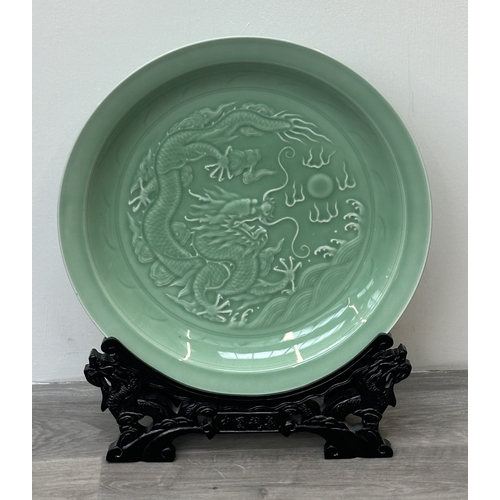89 - A Chinese celadon glazed ceramic charger with dragon motif on carved wooden stand - approx. 50cm dia... 