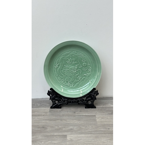 89 - A Chinese celadon glazed ceramic charger with dragon motif on carved wooden stand - approx. 50cm dia... 