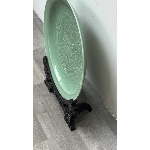 89 - A Chinese celadon glazed ceramic charger with dragon motif on carved wooden stand - approx. 50cm dia... 