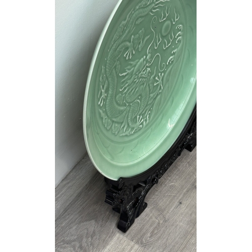 89 - A Chinese celadon glazed ceramic charger with dragon motif on carved wooden stand - approx. 50cm dia... 