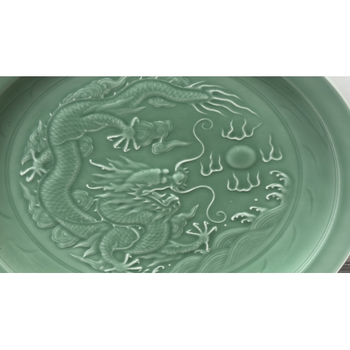 89 - A Chinese celadon glazed ceramic charger with dragon motif on carved wooden stand - approx. 50cm dia... 