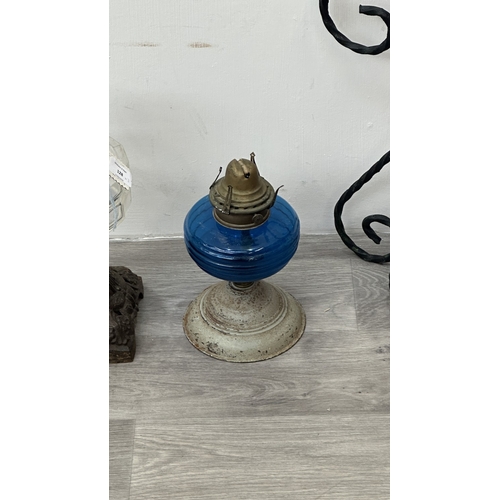 128 - Three oil lamps, one cranberry glass and brass on wrought metal stand, one British made metal and bl... 