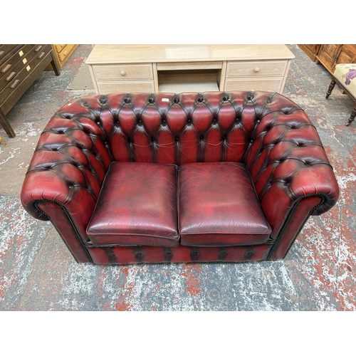 173 - An oxblood leather Chesterfield two-seater sofa - approx. 76cm high x 140cm wide x 75cm deep